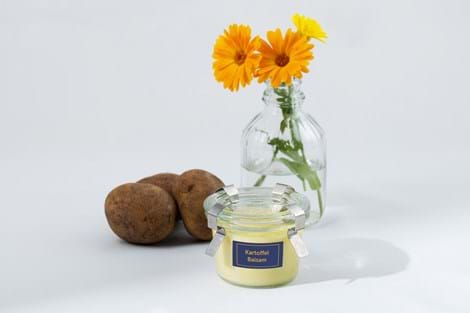Kartoffelbalsam in kleinem Glas vor Kartoffeln und Ringelblumen in kleiner Vase