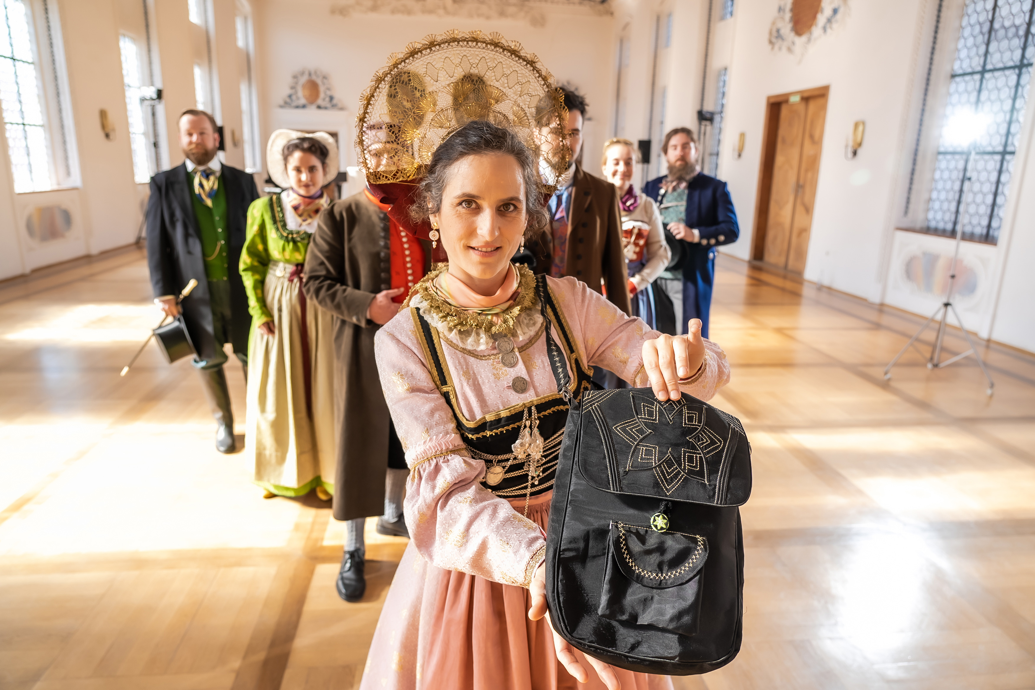 Eine Frau in rosa Tracht hält eine schwarze Tasche.