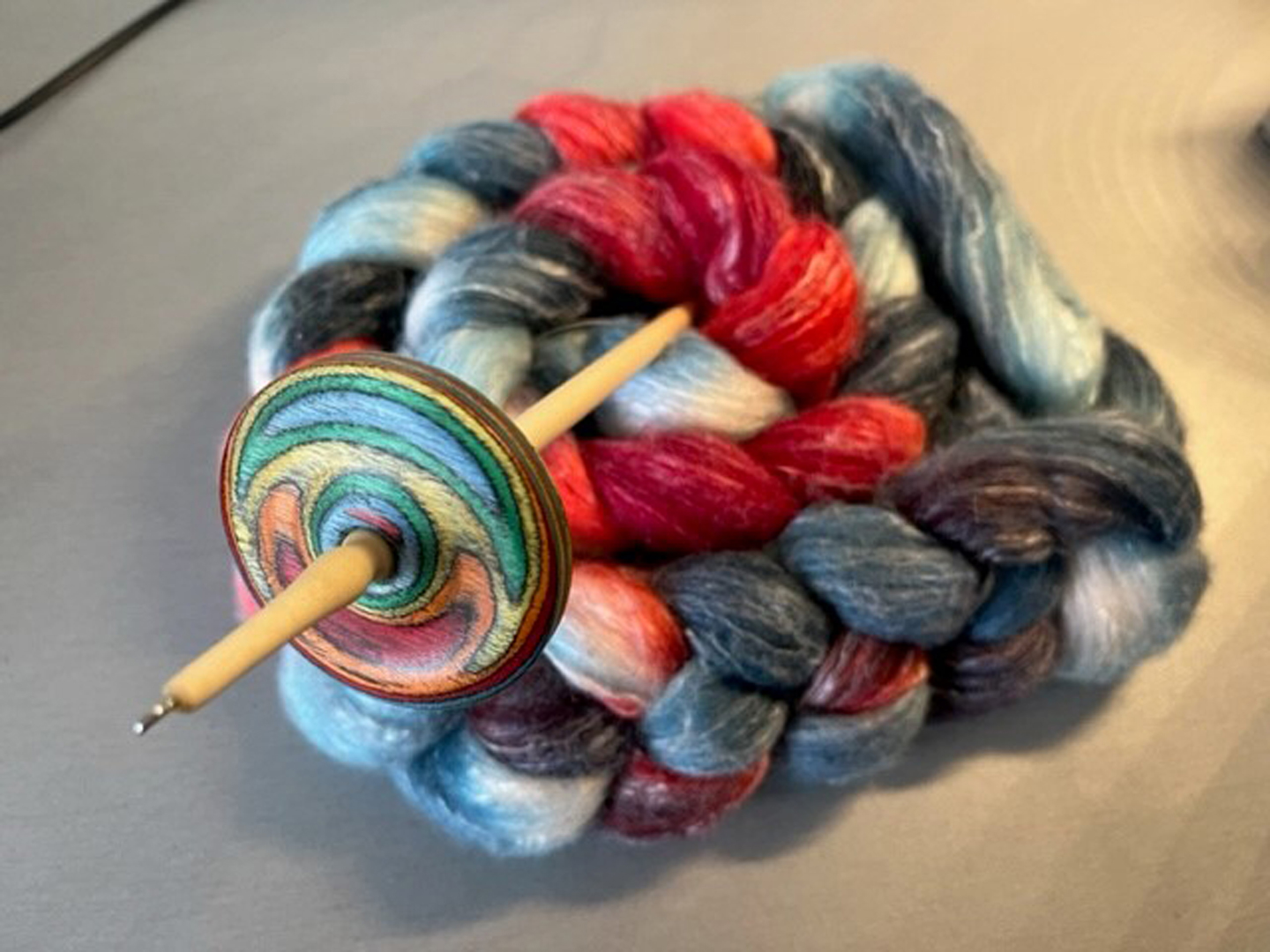 Bunt gefärbte Wolle und eine Handspindel.