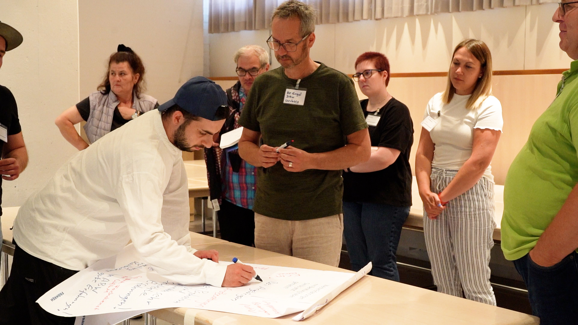 ein junger Mann schreibt auf ein Flipchart, um ihn weitere Personen