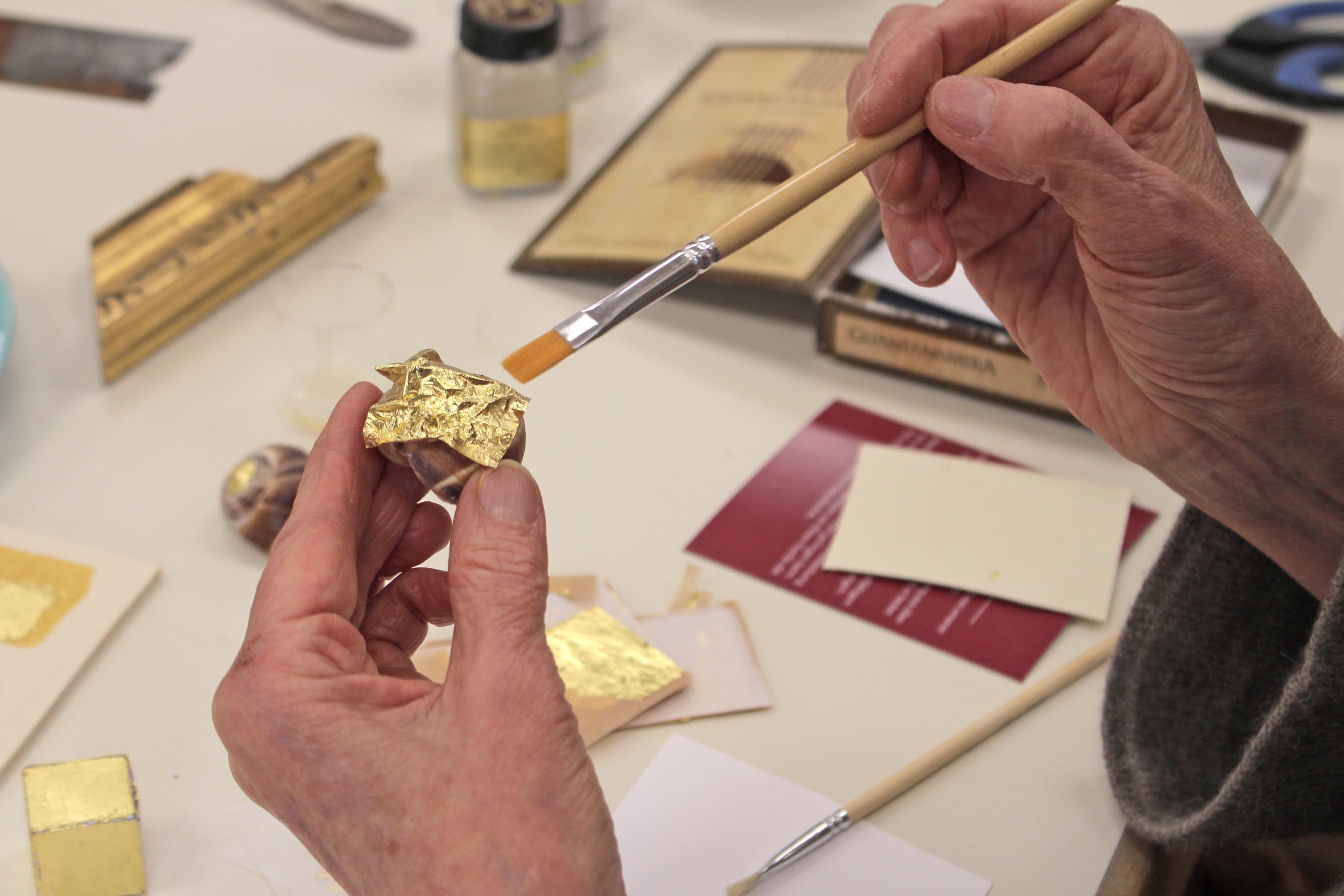 Hände halten Pinsel und kleines Objekt mit Goldplättchen