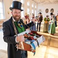 Ein Mann mit Bauchladen und eine Gruppe von Menschen in Tracht.