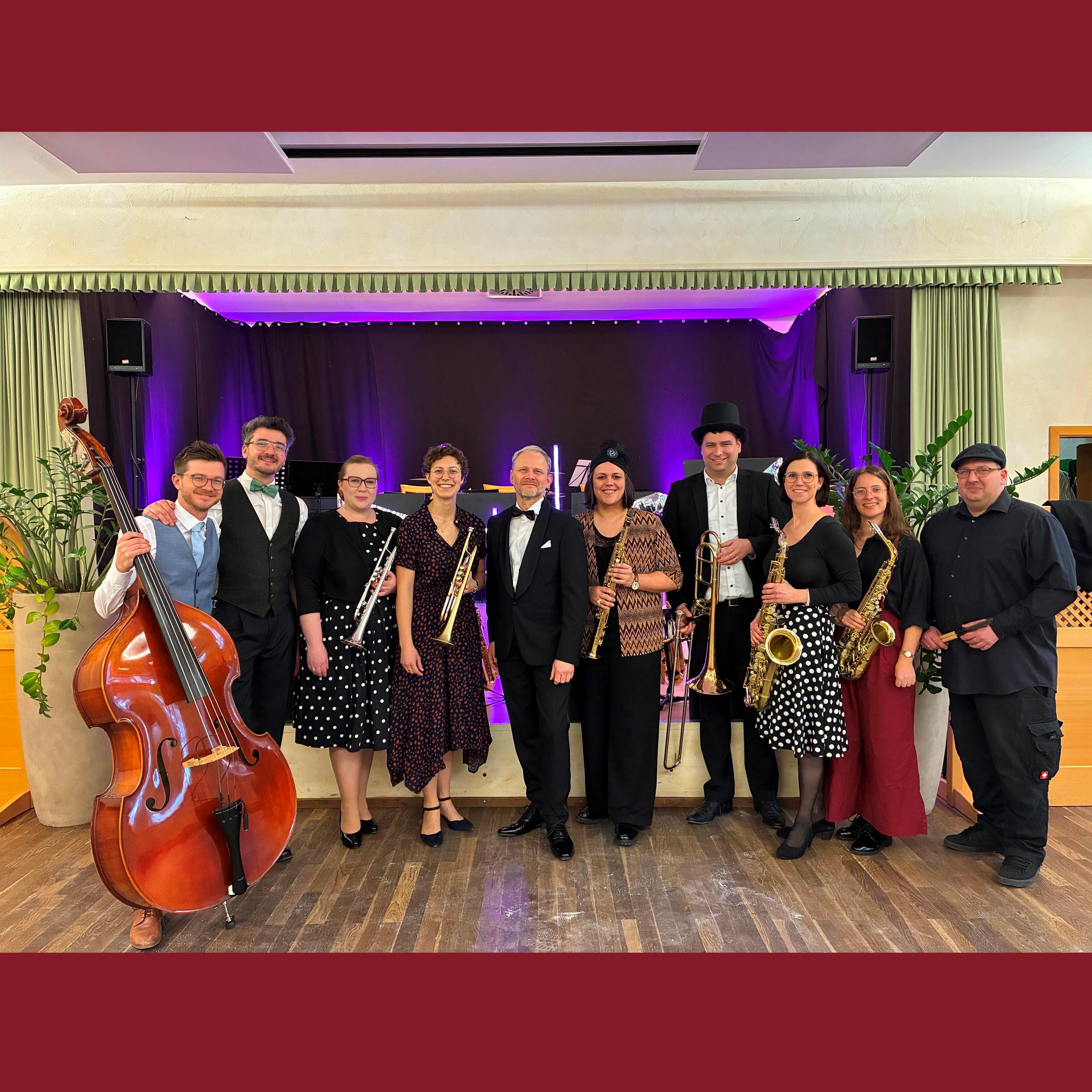 Gruppe von 10 Musikern mit Instrumenten mit Bühne im Hintergund
