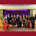 Gruppe von 10 Musikern mit Instrumenten mit Bühne im Hintergund