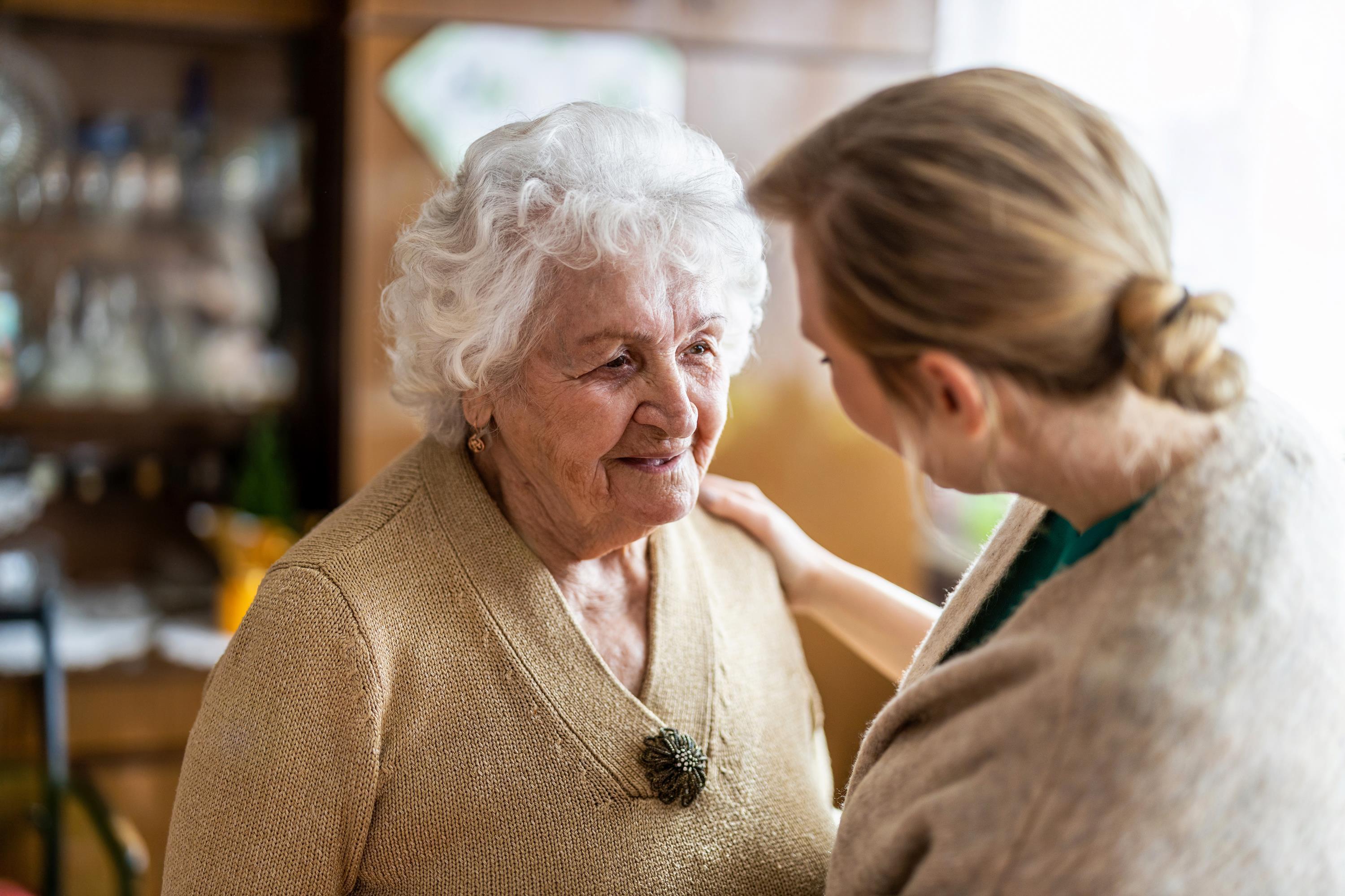 Seniorin lächelt eine Frau an, diese legt eine Hand auf ihre Schulter