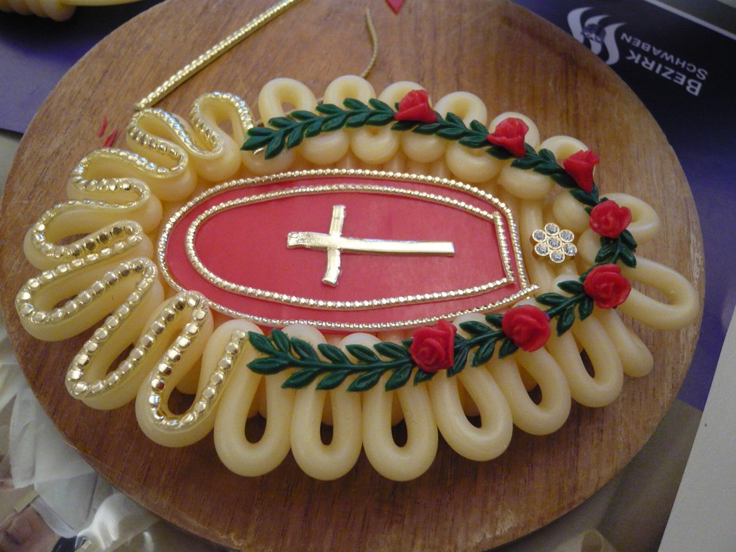 ein aus Wachs hergestellter Kranz, in der Mitte ein goldenes Kreuz