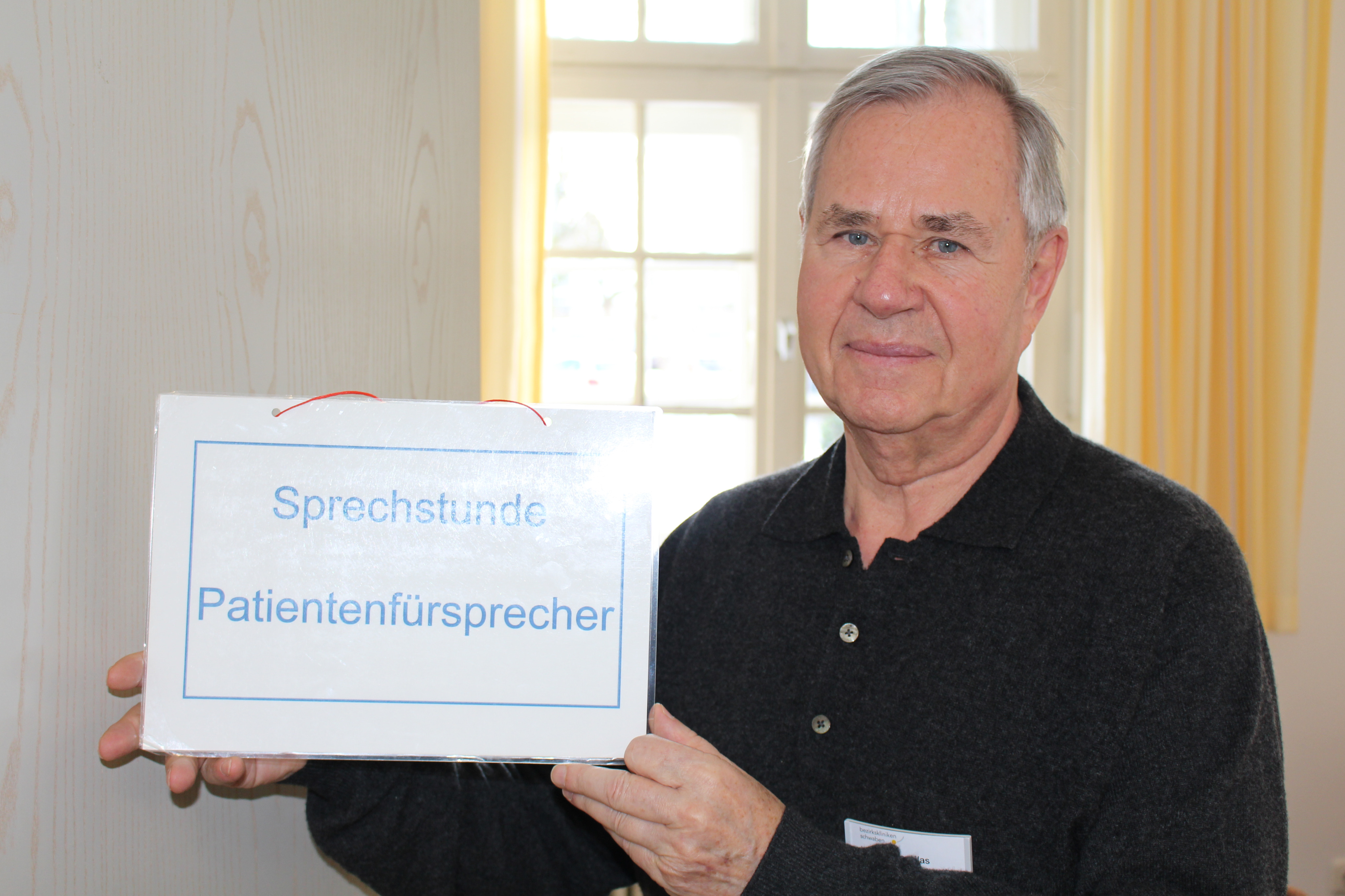 Herr Klas hält ein Schild mit der Aufschrift Sprechstunde Patientenfürsprecher in den Händen