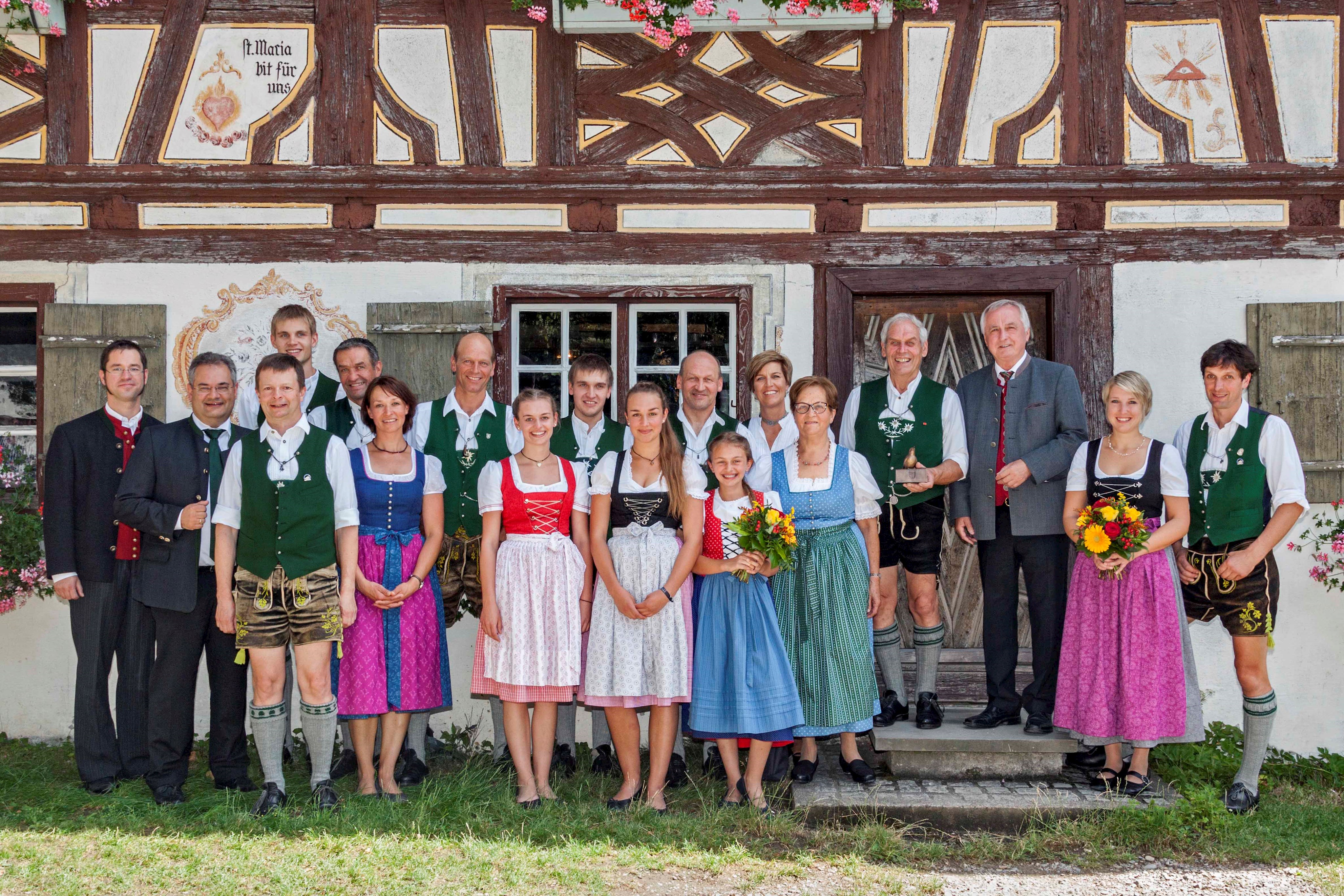 Gruppenbild der Familie Wechs zusammen mit Bezirkstagspräsident Jürgen Reichert (Dritter von rechts), Bezirksrat Edgar Rölz (Zweiter von links) und Volksmusikberater Christoph Lambertz (Erster von links). Die Familie Wechs trägt Trachtenkleidung; im Hintergrund ist eines der historischen Gebäude im Schwäbischen Bauernhofmuseum Illerbeuren zu sehen.