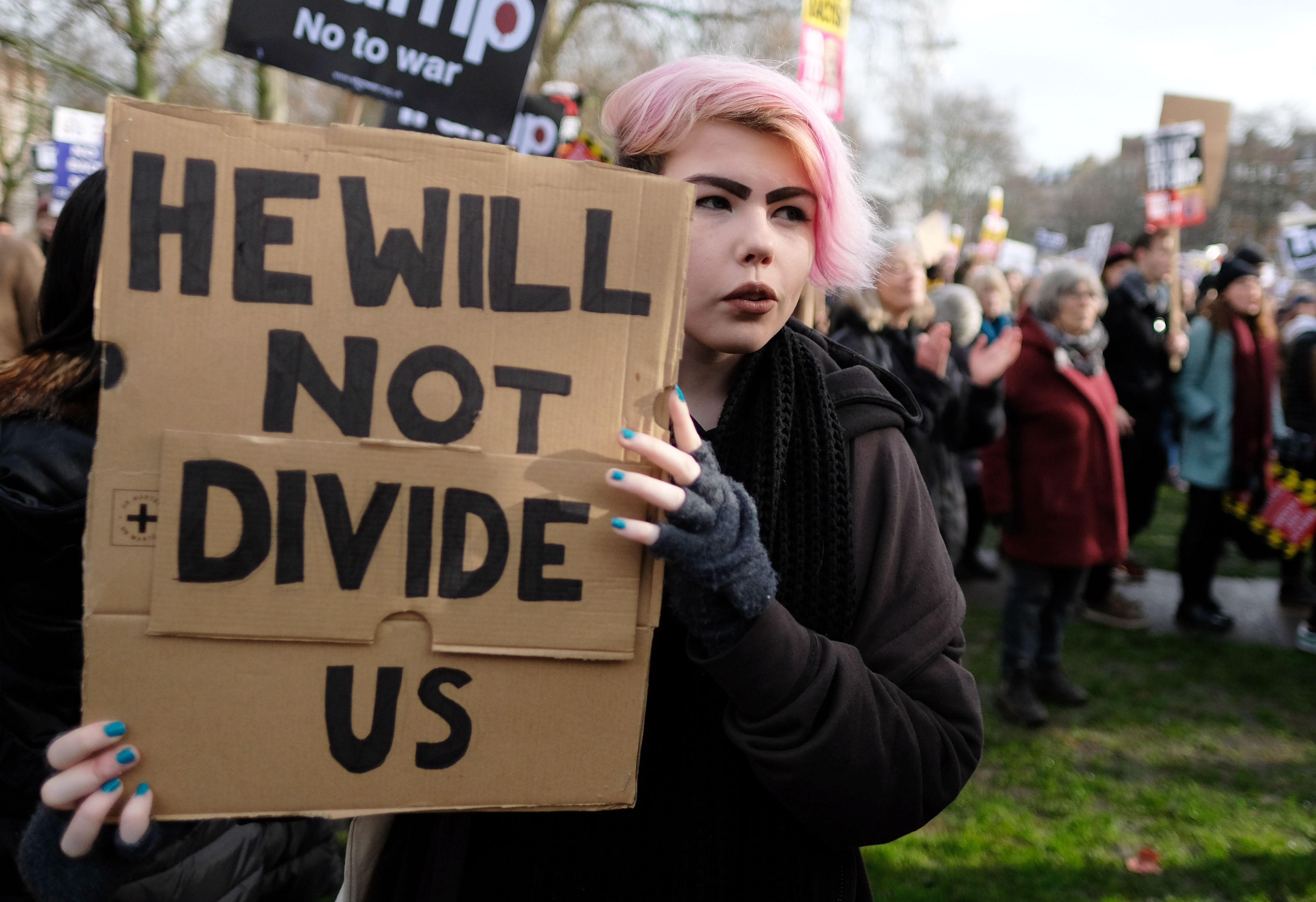 Eine junge Frau hält ein Pappschild mit dem Text: He will not divide us. (Er wird uns nicht spalten.)