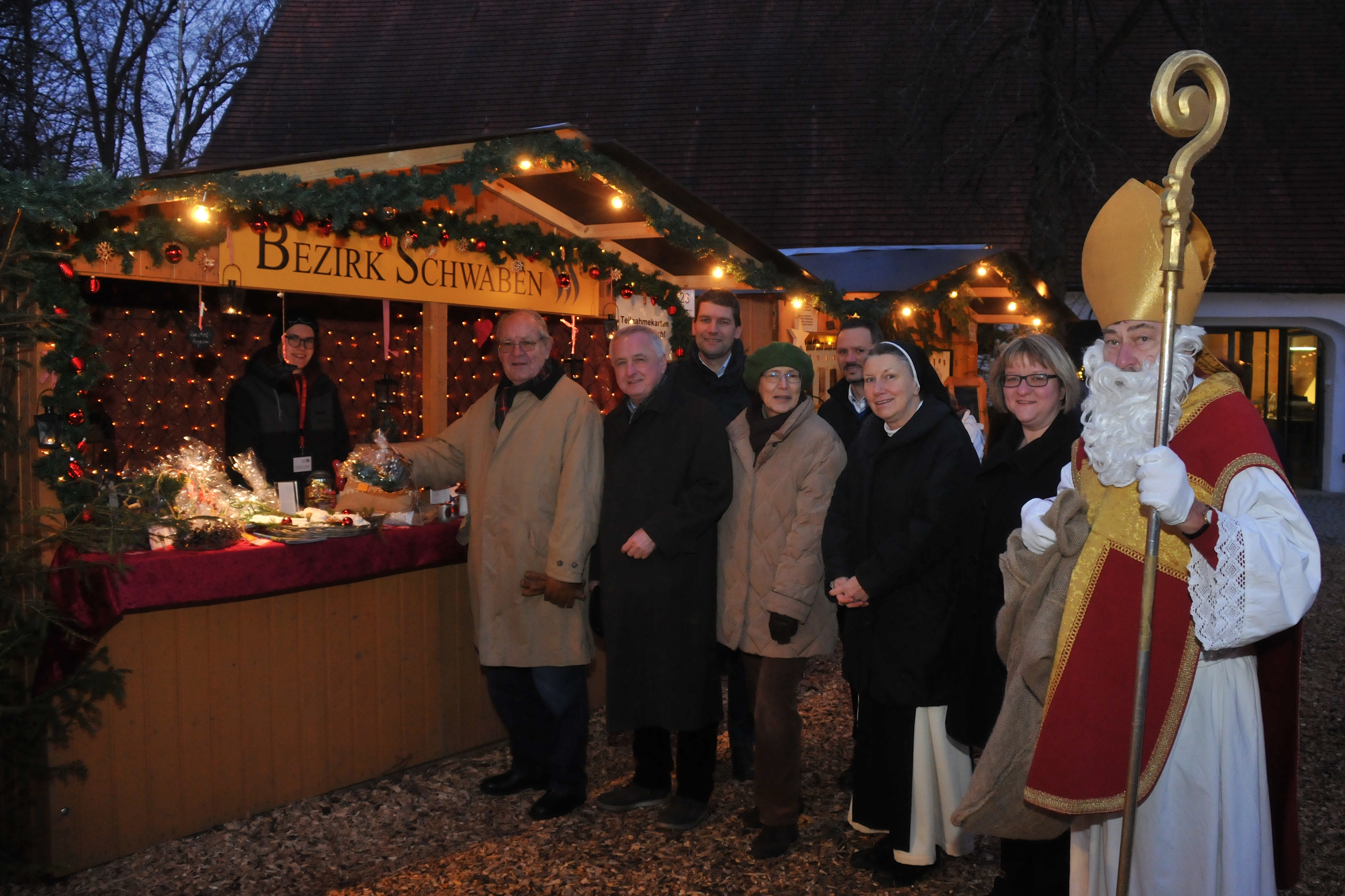 Der „Heilige Nikolaus“ besucht am Oberschönenfelder Weihnachtsmarkt den Bezirksstand: v. l.: Bezirksrat Manfred Buhl, Bezirkstagspräsident Jürgen Reichert, Verwaltungsdirektor des Bezirks Schwaben Dr. Georg Bruckmeir, Leiterin des Volkskundemuseums Dr. Beate Spiegel, Erster Bürgermeister der Gemeinde Gessertshausen Jürgen Mögele, Äbtissin Schwester M. Gertrud Pesch, Kreisheimatpflegerin Claudia Ried.