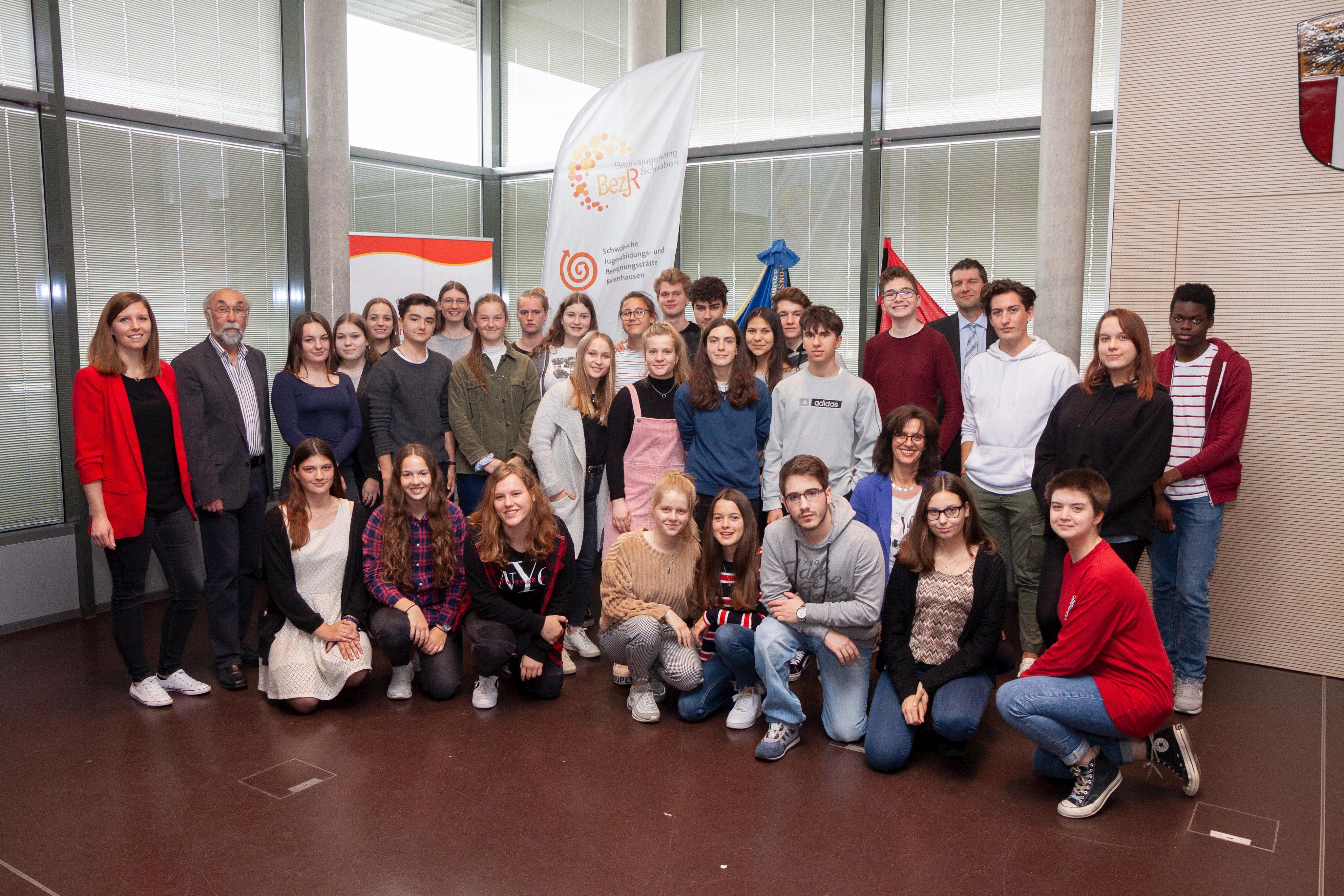 Gruppenbild der Jugendlichen der 10. Klasse des Maria-Theresia-Gymnasiums in Augsburg gemeinsam mit der Jugendbeauftragten des Schwäbischen Bezirkstags, Renate Deniffel (kniend, 3.v.r.), Bezirksrat Wolfgang Bähner (stehend, 2.v.l.) und dem Direktor der Bezirksverwaltung, Dr. Georg Bruckmeir (stehend, 4.v.r.).