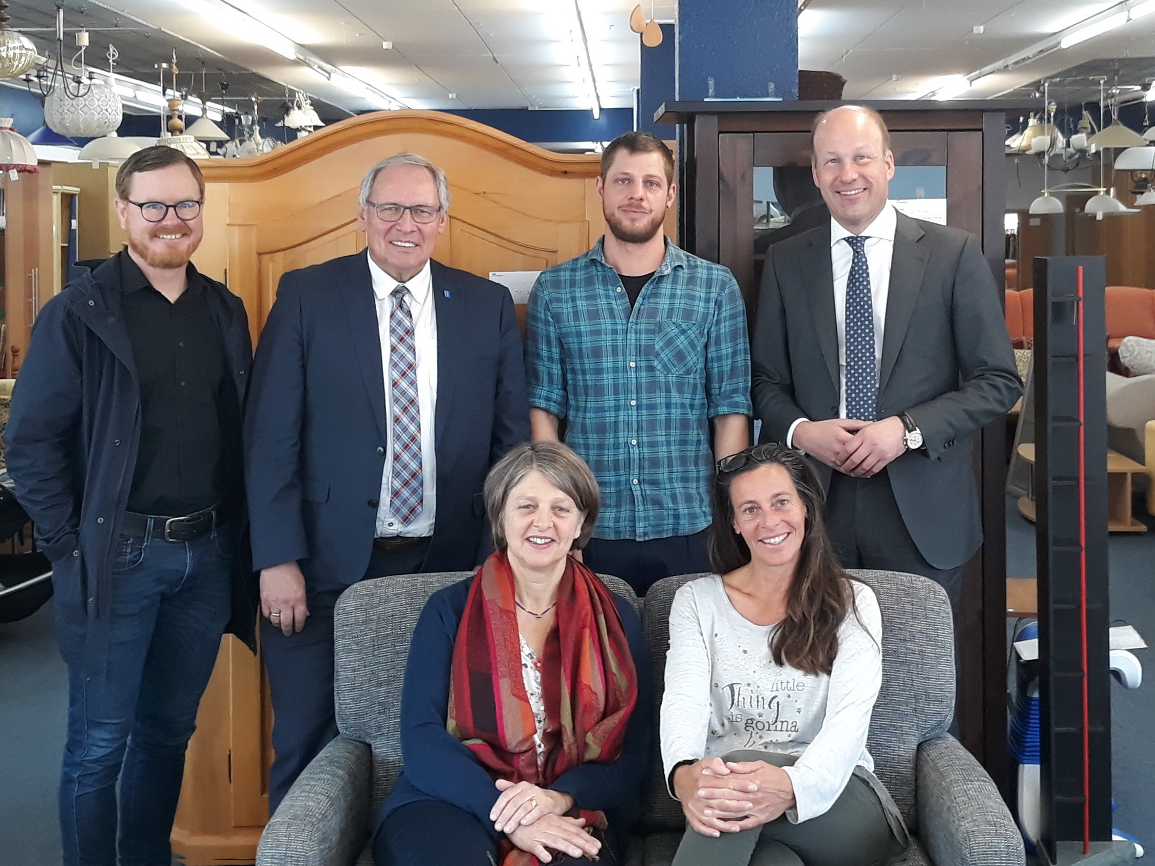 Das Foto zeigt auf dem Sofa  Barbara Holzmann (links) und Johanna Weinzierl. Dahinter stehen (v.l.) Andreas Breuer, Landrat Anton Klotz, Jan Alt (Mitarbeiter im Möbelhaus), Bezirkstagspräsident Martin Sailer.