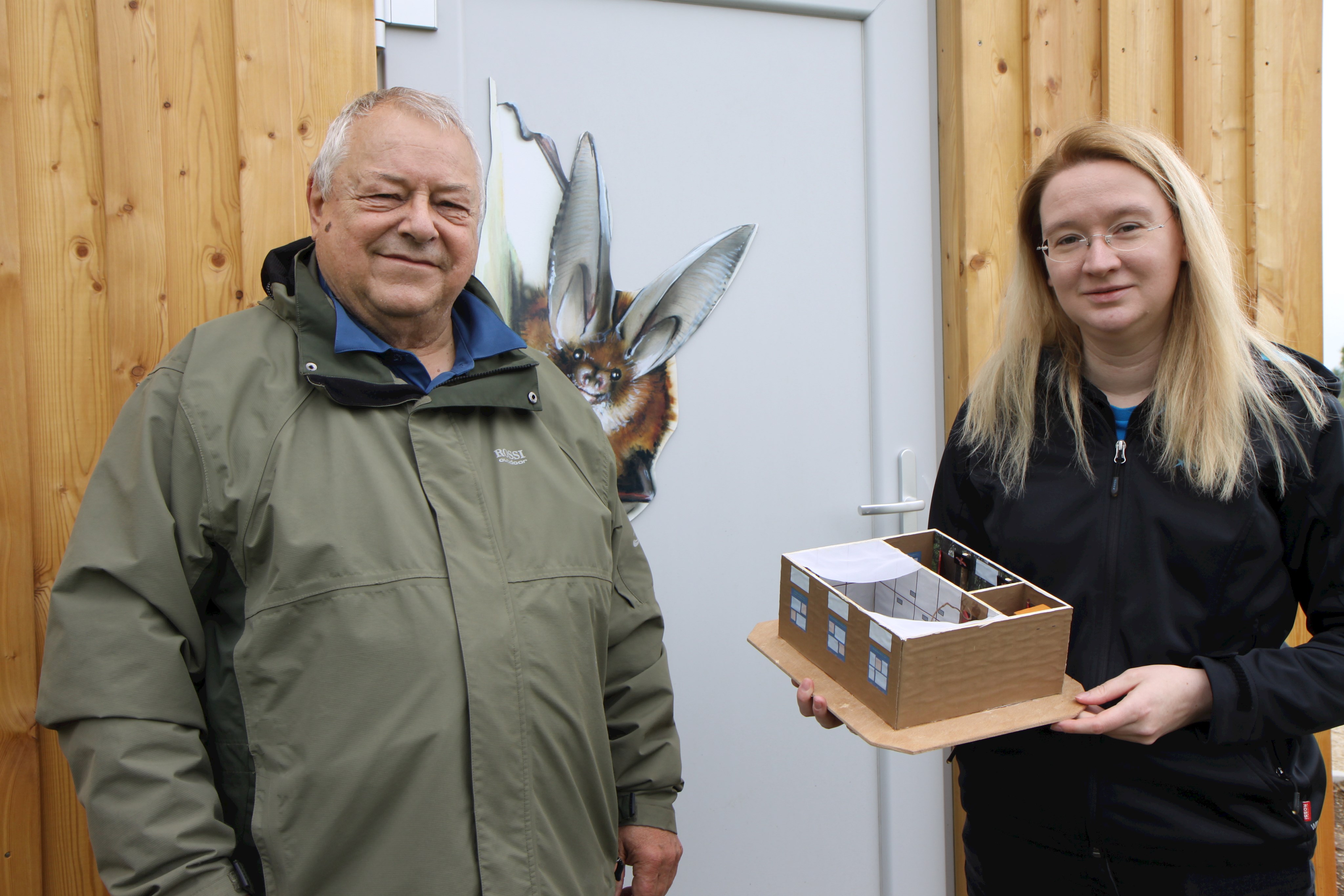 Claudia Weißschädel vom Fledermausschutz Augsburg hält ein Modell der Auffangstation in den Händen, neben ihr steht Günther Groß; auf der Wand im Hintergrund ist eine Fledermaus aufgemalt