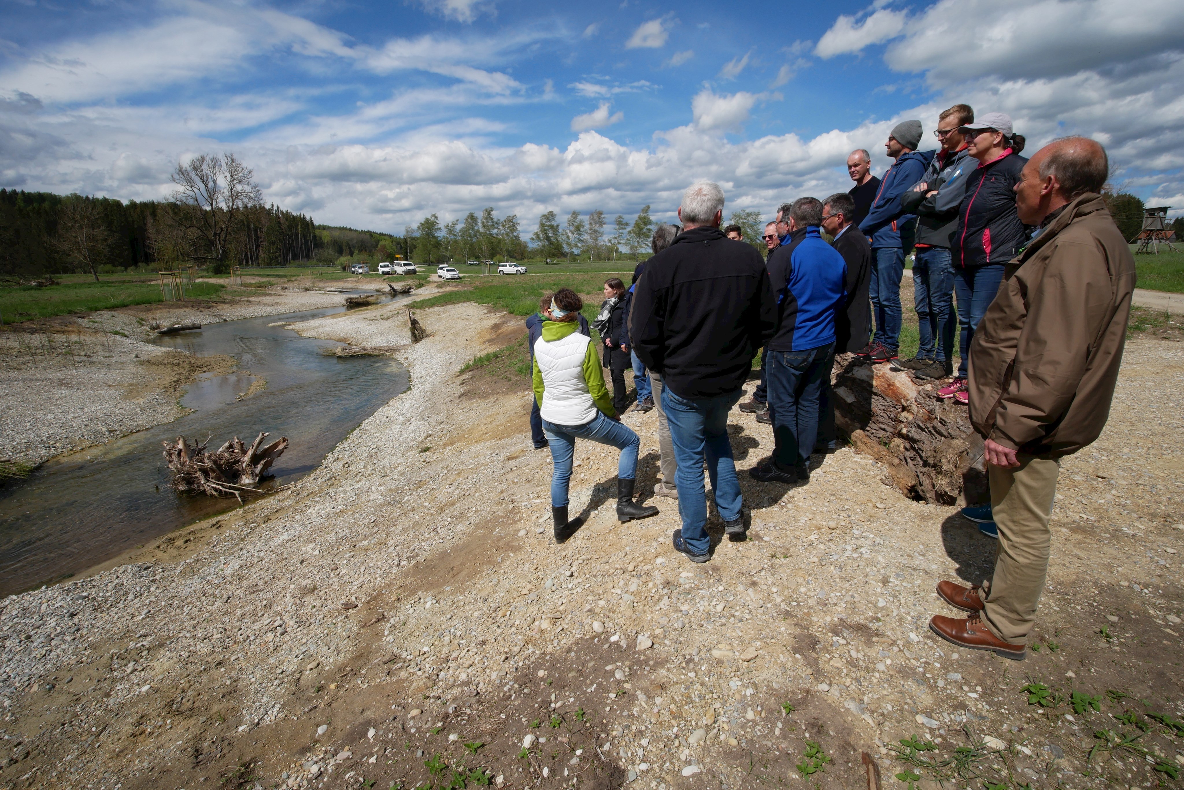 Die Gruppe der Teilnehmer steht an einem gewundenen Flusslauf, in dem Wurzelstöcke eingebracht sind.