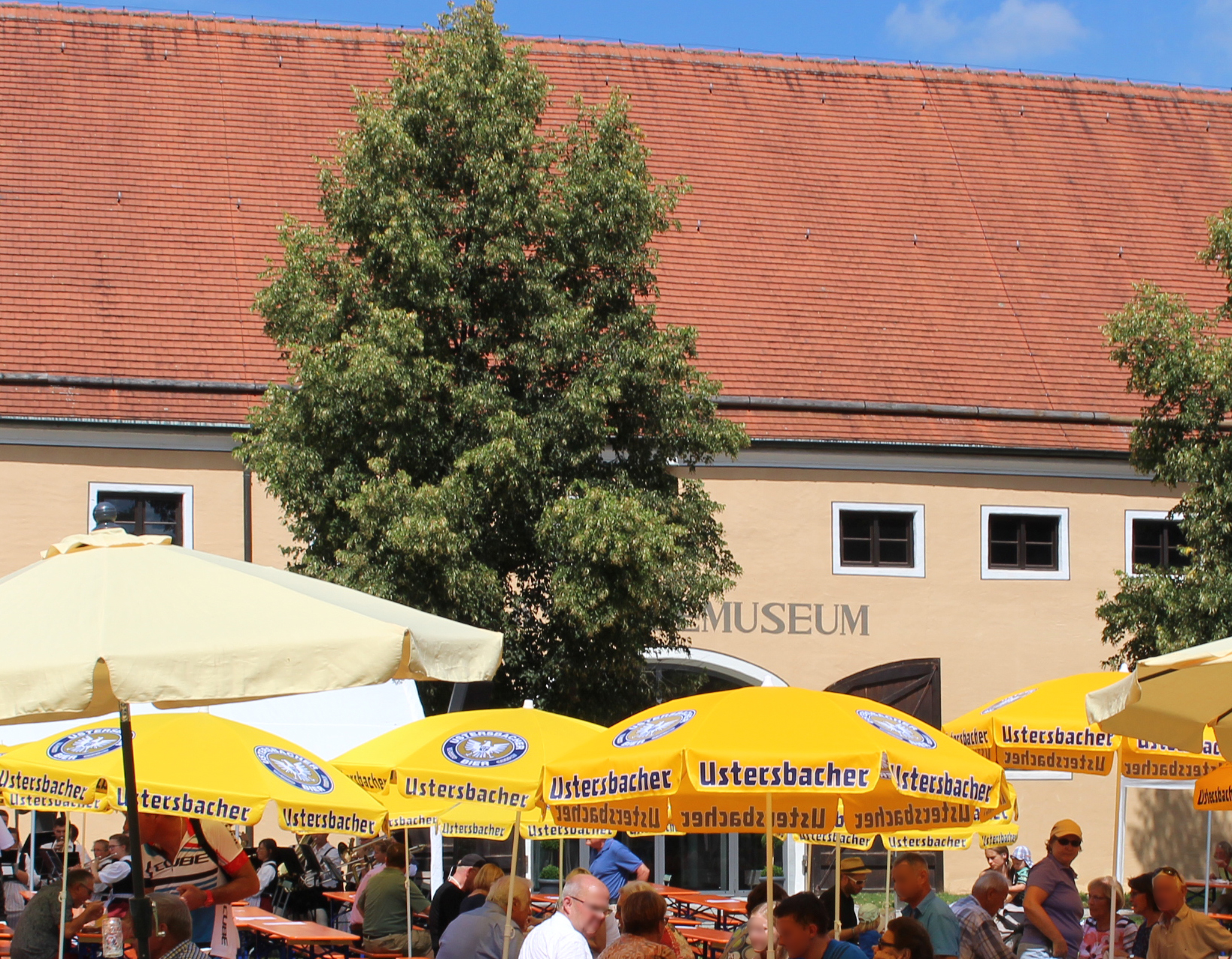 Gelbe Sonnenschirme und Bierbänke mit vielen Menschen im Museumshof