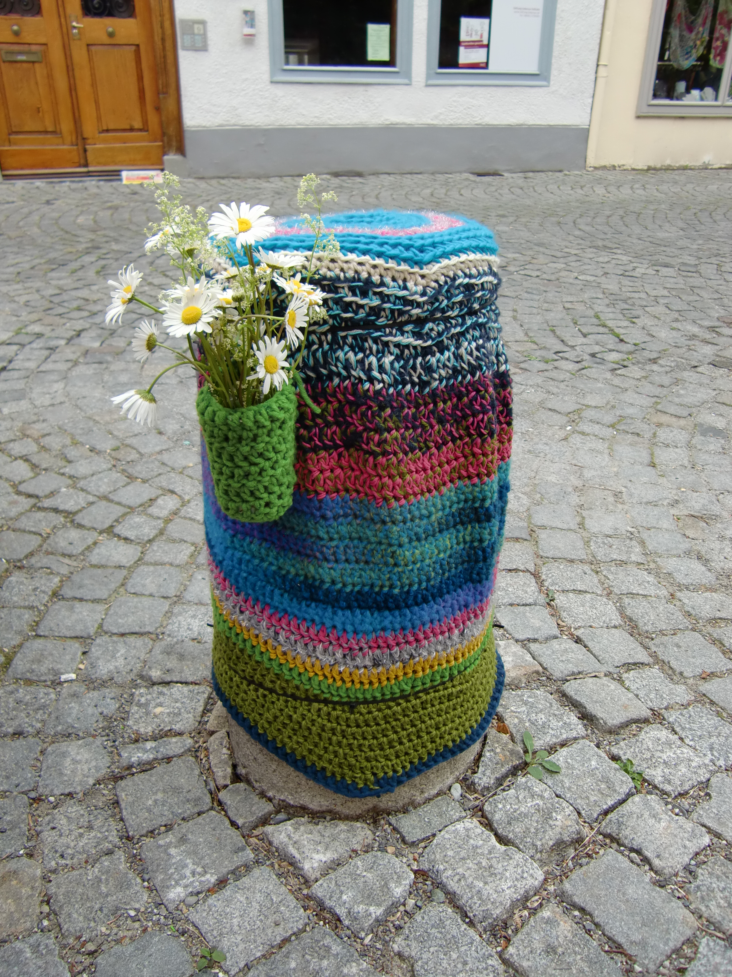 Nach den ersten Spenden kommen nun auch solidarische Aktionen dazu. Das Team der Tagesklinik weiß zwar nicht, wer den Poller vor der Galerie umhäkelt und mit einer Blumenvase versehen hat, aber die Mitarbeiterinnen und Mitarbeiter finden es klasse.