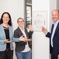 Gleichstellungsbeauftragte Nadja Hein (links), Birgit Zeitz von der Personalverwaltung und Bezirkstagspräsident Martin Sailer freuen sich über das Zertifikat von audit berufundfamilie im Hauptgebäude des Bezirks Schwaben in Augsburg.