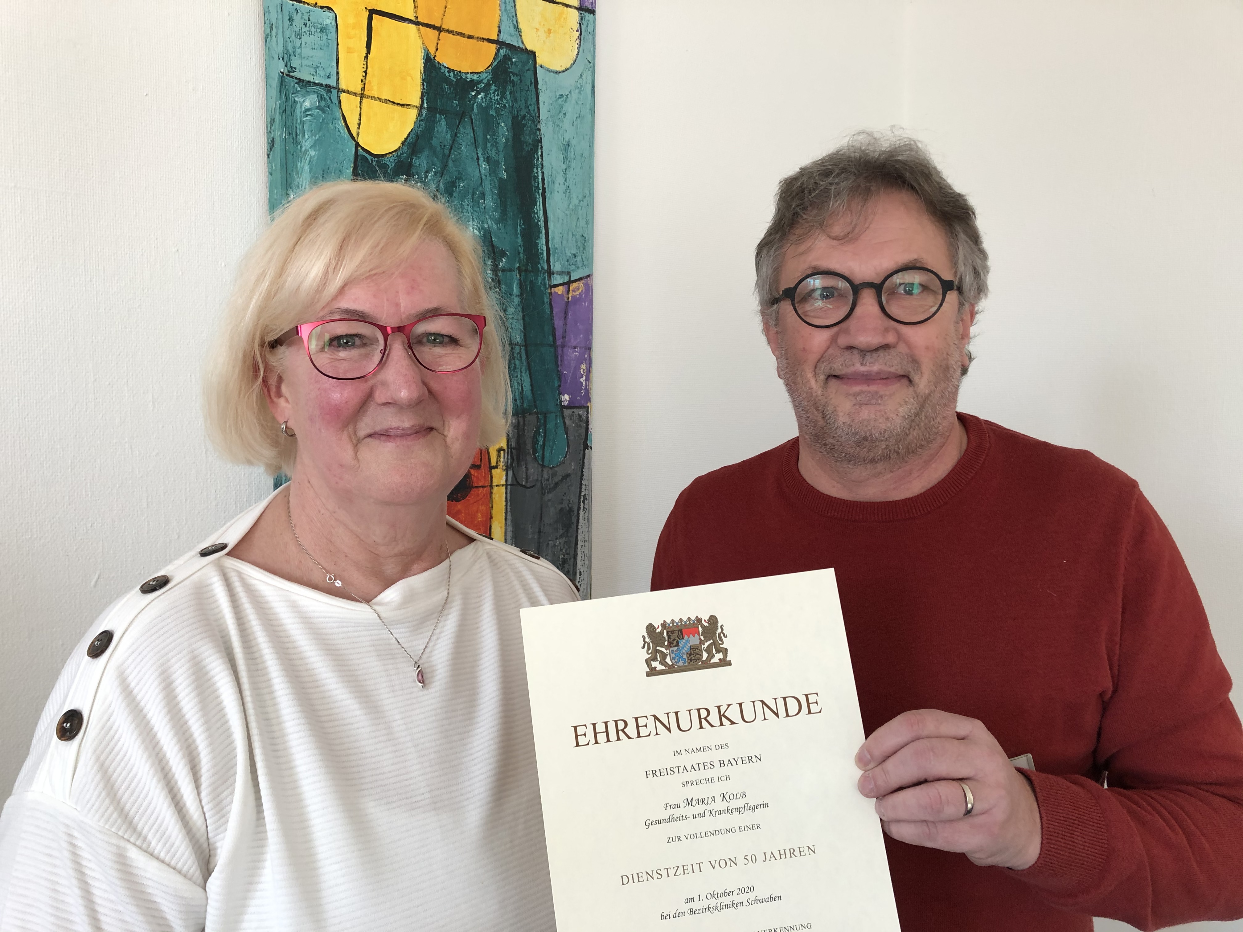 Pflegedirektor Harald Keller überreicht Maria Kolb eine Ehrenurkunde des Freistaates Bayern. Sie arbeitet seit 50 Jahren im Bezirkskrankenhaus Kaufbeuren. Am Freitag ist ihr letzter Arbeitstag.
