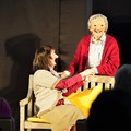 Zwei Schauspielende mit Gesichtsmasken halten Händchen.
